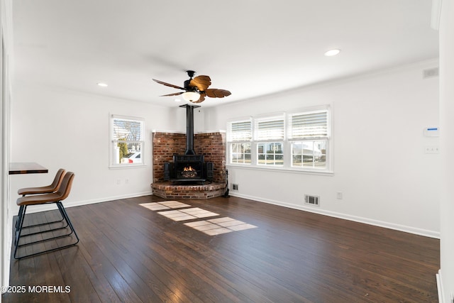 unfurnished living room featuring a wood stove, baseboards, dark wood-style flooring, and crown molding