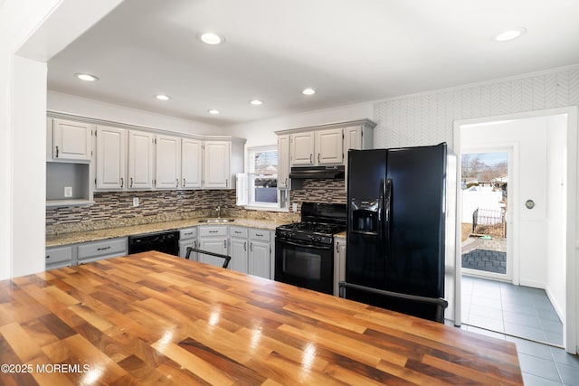 kitchen with recessed lighting, black appliances, under cabinet range hood, tile patterned floors, and butcher block counters