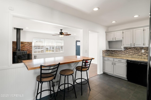 kitchen featuring a breakfast bar, black dishwasher, butcher block counters, decorative backsplash, and a wood stove