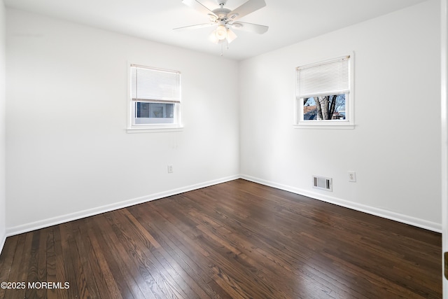 empty room with dark wood-style floors, visible vents, a ceiling fan, and baseboards