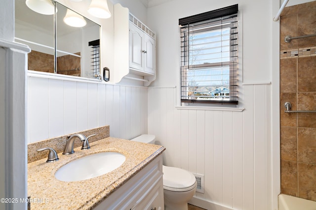 full bath with a tile shower, a wainscoted wall, toilet, and vanity