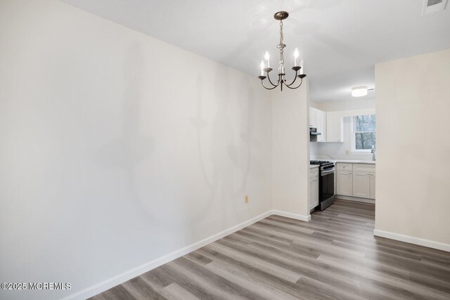 unfurnished dining area with a notable chandelier, visible vents, light wood-style floors, and baseboards