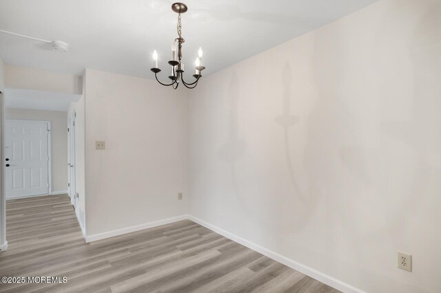 unfurnished dining area with light wood finished floors, a chandelier, and baseboards