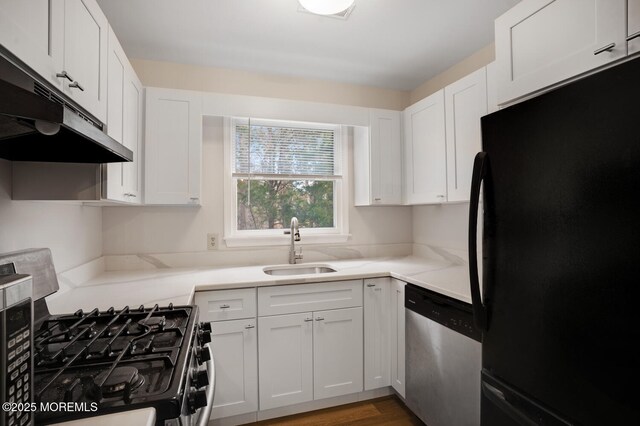 kitchen featuring a sink, under cabinet range hood, freestanding refrigerator, gas range, and dishwasher