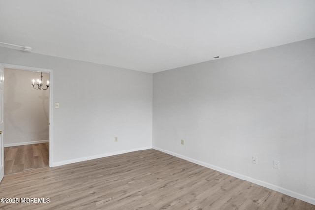 unfurnished room with a chandelier, baseboards, and wood finished floors