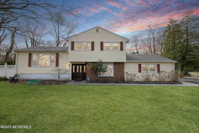 split level home featuring a front lawn, fence, and brick siding