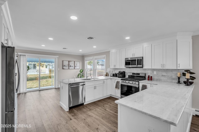 kitchen featuring a sink, backsplash, appliances with stainless steel finishes, a peninsula, and crown molding