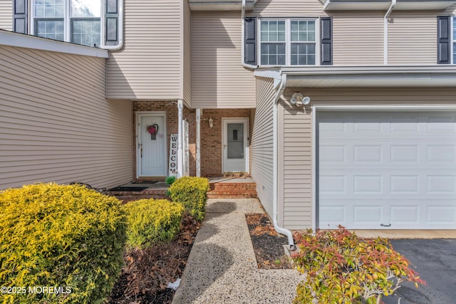 view of exterior entry featuring a garage and brick siding