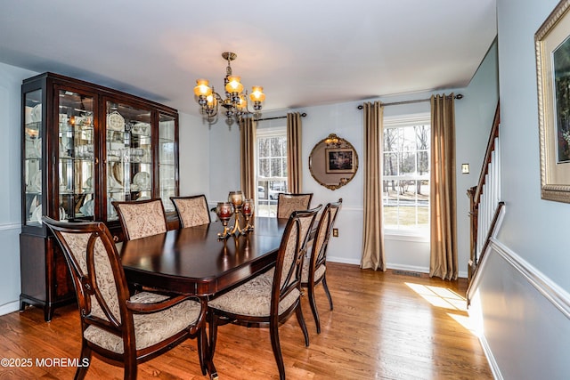 dining space with stairway, baseboards, an inviting chandelier, and wood finished floors