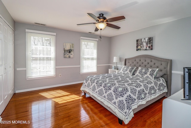 bedroom with visible vents, wood finished floors, a closet, baseboards, and ceiling fan