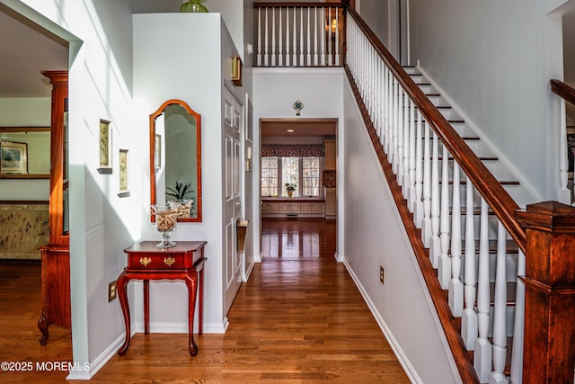 interior space with stairs, a high ceiling, baseboards, and wood finished floors