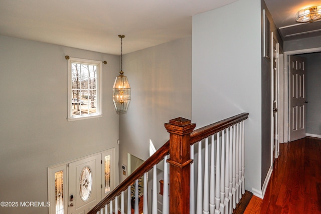 corridor with baseboards, an inviting chandelier, an upstairs landing, and dark wood-style flooring