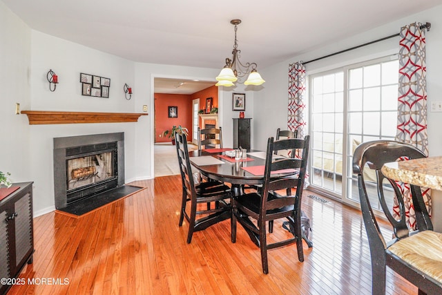 dining area featuring a notable chandelier, a fireplace with flush hearth, light wood-style floors, and visible vents