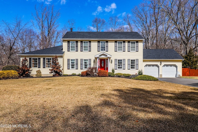 colonial home with aphalt driveway, a garage, a front lawn, and fence