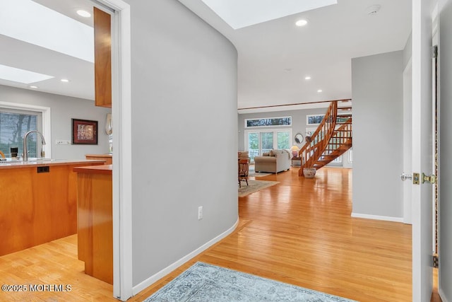 corridor with light wood-type flooring, a sink, a skylight, baseboards, and stairs