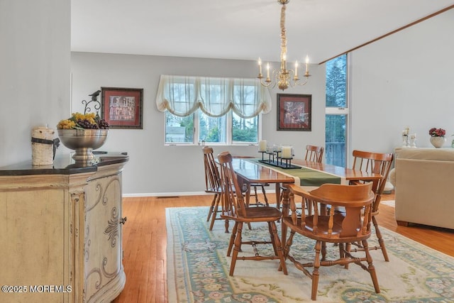 dining area with light wood-style flooring, a notable chandelier, and baseboards