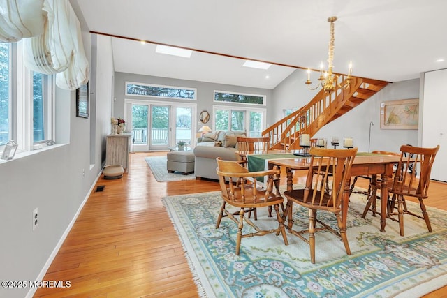 dining space with stairway, vaulted ceiling with skylight, light wood-type flooring, and baseboards