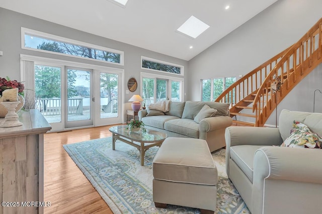 living room featuring high vaulted ceiling, recessed lighting, light wood-style floors, a skylight, and stairs