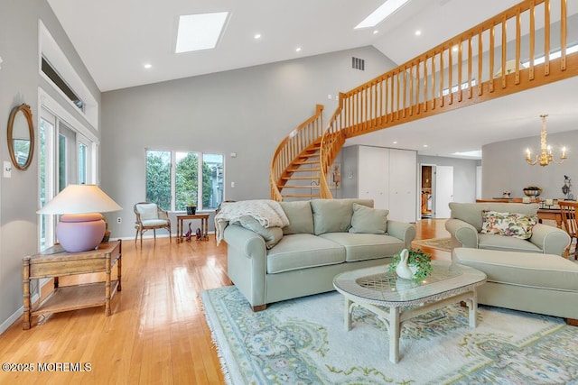 living room featuring visible vents, high vaulted ceiling, a skylight, a chandelier, and stairs