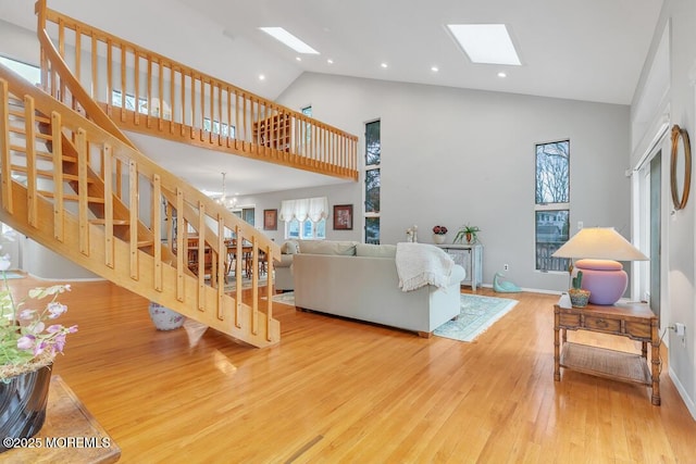 living room with stairway, a skylight, an inviting chandelier, wood finished floors, and high vaulted ceiling