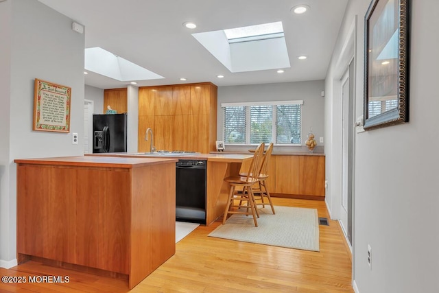 kitchen featuring light wood finished floors, a peninsula, a skylight, black appliances, and modern cabinets