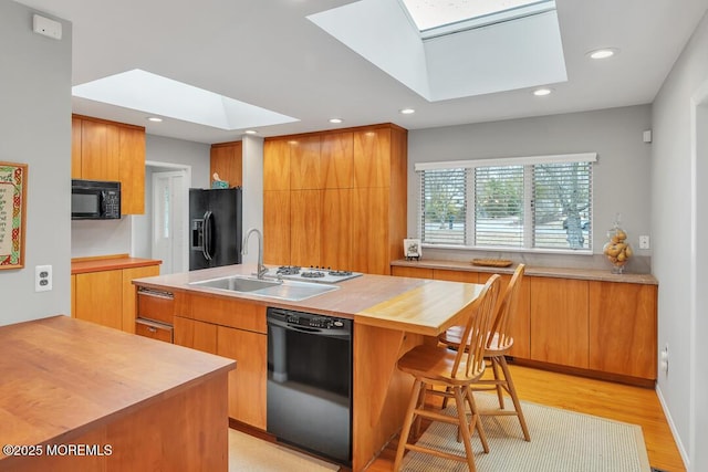 kitchen with wooden counters, a skylight, a sink, black appliances, and modern cabinets