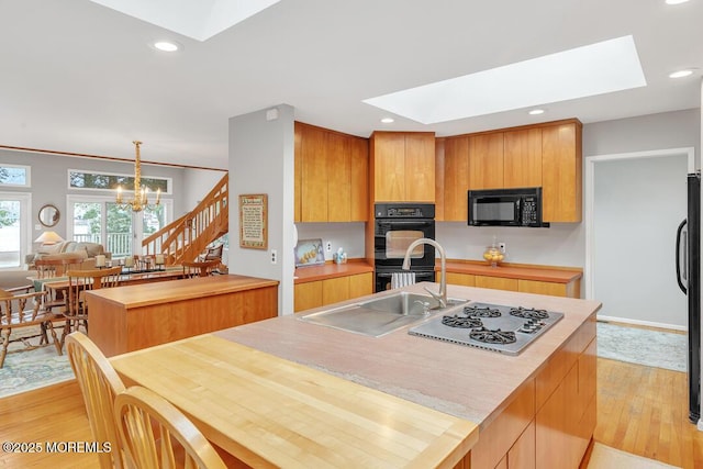 kitchen with a skylight, black appliances, light wood-type flooring, and an inviting chandelier