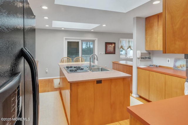 kitchen with an island with sink, a sink, freestanding refrigerator, stainless steel gas stovetop, and light countertops