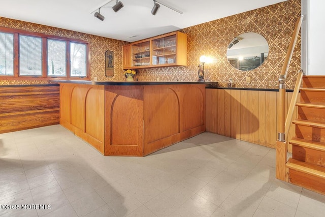 kitchen with brown cabinetry, light floors, a breakfast bar, glass insert cabinets, and dark countertops