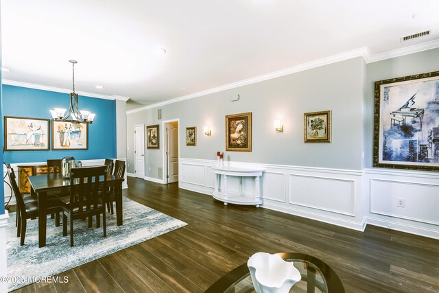 dining area with wood finished floors, visible vents, an inviting chandelier, wainscoting, and crown molding