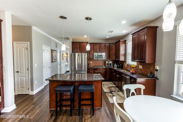 kitchen featuring a kitchen island, dark wood-type flooring, dark stone counters, decorative backsplash, and stainless steel appliances