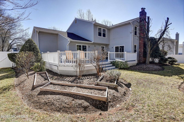 back of house with a chimney, fence, a yard, and a garden