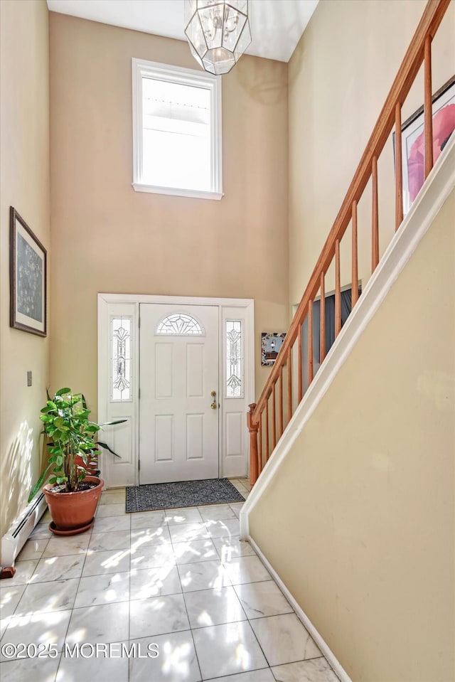 entryway featuring a high ceiling, tile patterned flooring, baseboard heating, a chandelier, and stairs