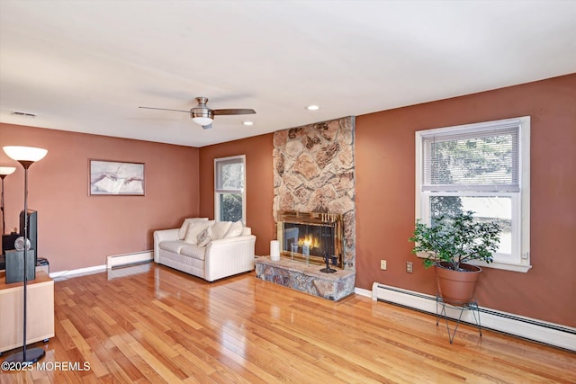 living room featuring light wood finished floors, visible vents, a baseboard heating unit, a stone fireplace, and a baseboard radiator