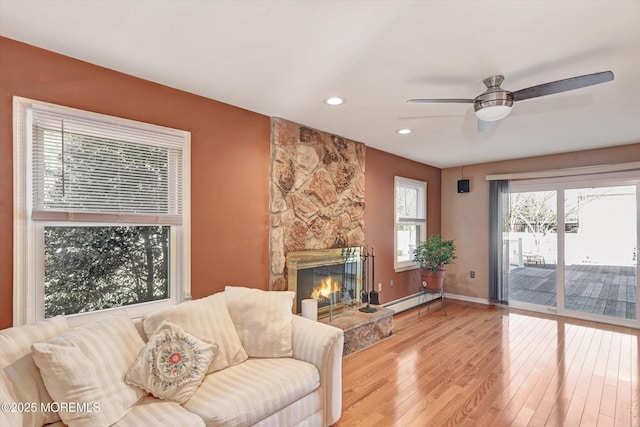 living area with baseboards, a stone fireplace, recessed lighting, wood finished floors, and a baseboard radiator