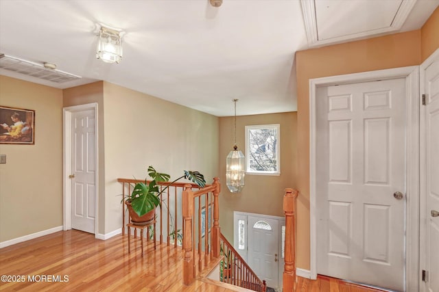 hallway with an upstairs landing, attic access, baseboards, and light wood-style floors