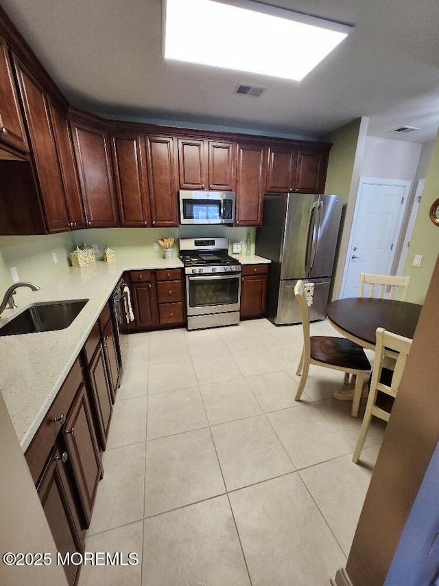 kitchen featuring visible vents, a sink, light stone counters, stainless steel appliances, and light tile patterned floors