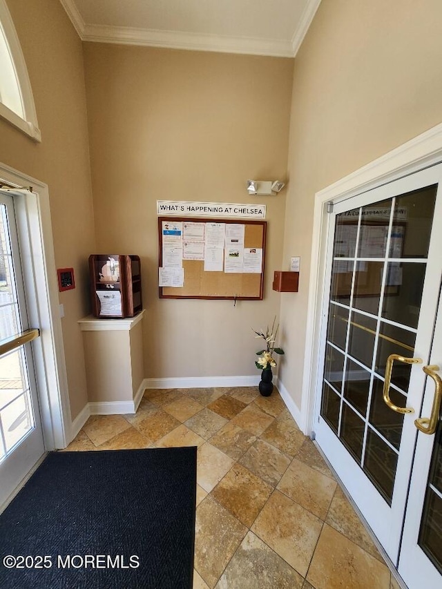 interior space featuring stone finish floor, baseboards, a towering ceiling, and ornamental molding