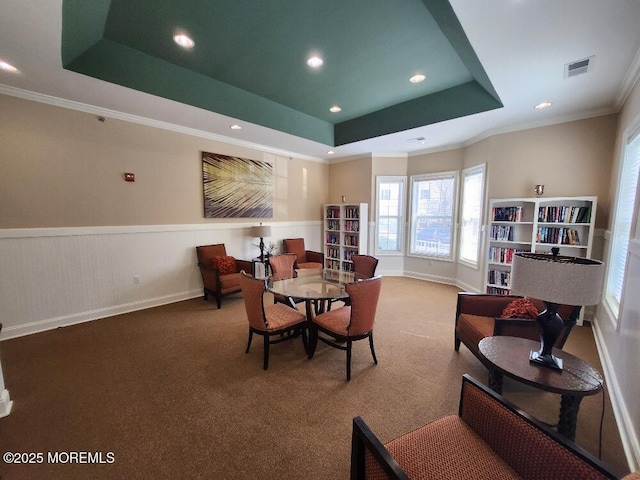 carpeted dining area featuring a raised ceiling, crown molding, visible vents, and wainscoting