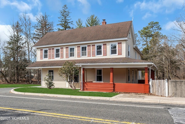 view of front of property with a front yard, fence, covered porch, a chimney, and a shingled roof