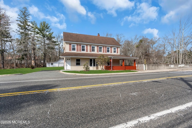 view of front of property with a porch, fence, roof with shingles, a front yard, and a chimney