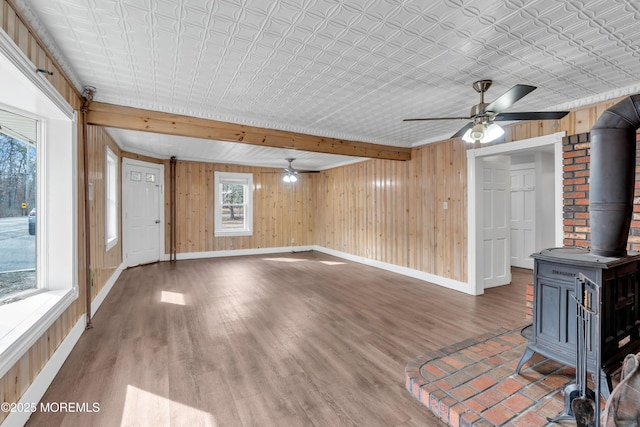 unfurnished living room featuring wooden walls, baseboards, a wood stove, wood finished floors, and a ceiling fan