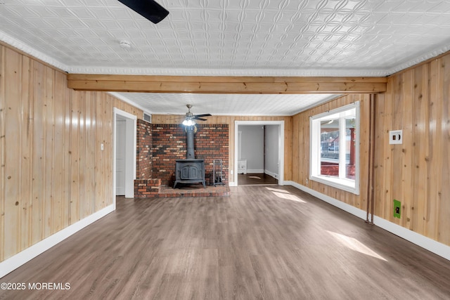 unfurnished living room featuring wooden walls, baseboards, a wood stove, wood finished floors, and an ornate ceiling