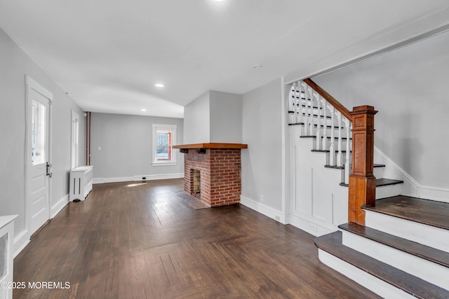 unfurnished living room with stairway, a brick fireplace, radiator heating unit, and baseboards