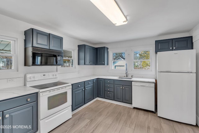 kitchen with a sink, white appliances, light wood-style flooring, and light stone countertops