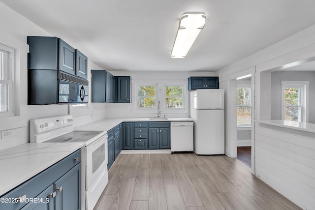 kitchen featuring white appliances, blue cabinetry, a wealth of natural light, and a sink