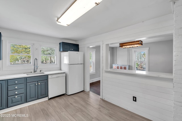 kitchen with blue cabinetry, light countertops, a wealth of natural light, white appliances, and a sink