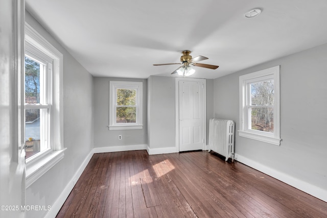 spare room featuring radiator, a ceiling fan, dark wood-type flooring, and baseboards