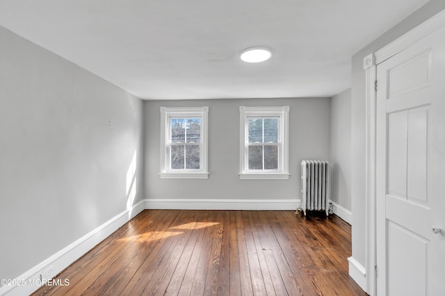 spare room with baseboards, dark wood-style floors, and radiator heating unit