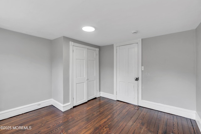 unfurnished bedroom featuring a closet, baseboards, and dark wood-style floors